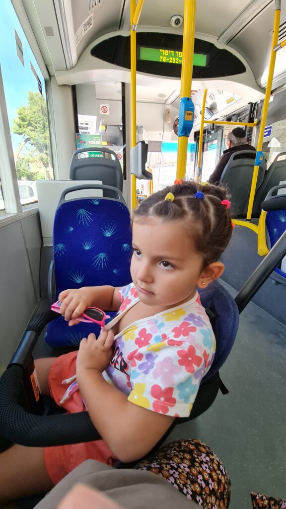 Nina desfrutando do lugar reservado para carrinhos ou cadeiras de rodas nos ônibus de Israel